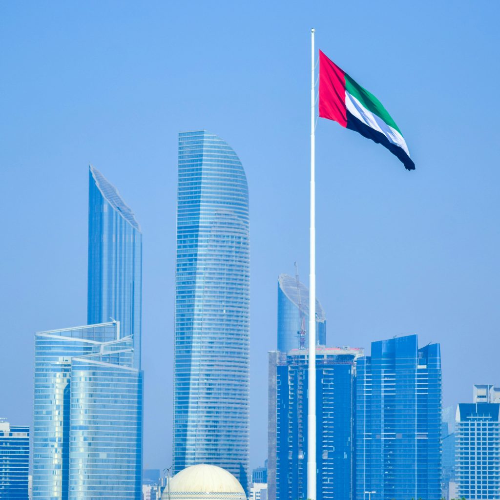 Modern skyline of UAE cityscape with national flag waving against clear sky.